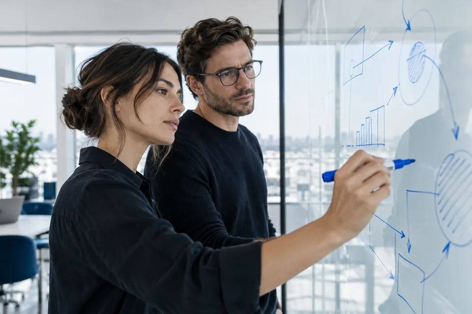 Colleagues sketching ideas on a glass board